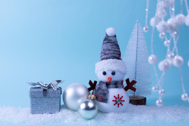 Boneco de neve, presente, árvore de Natal, bola de Natal na neve branca em um fundo turquesa