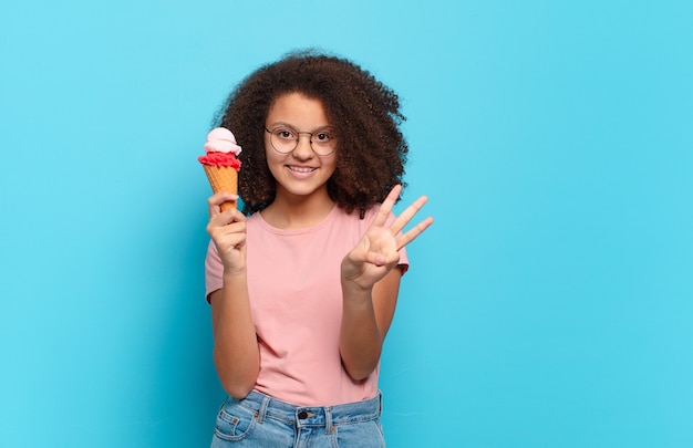 Bonita adolescente afro sonriendo y mirando amistosamente, mostrando el número tres o tercero con la mano hacia adelante, contando hacia atrás. concepto de helado de sumer