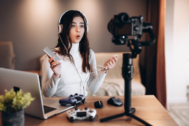 Bonita blogger sorprendida en auriculares está transmitiendo en vivo hablando de videojuegos. Influencer mujer joven transmisión en vivo mantenga power bank.