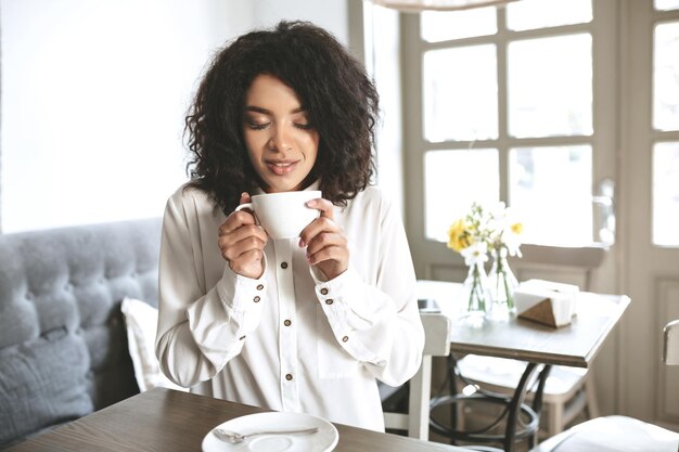 Bonita chica afroamericana sentada en un restaurante con una taza en las manos Joven bebiendo café en un café