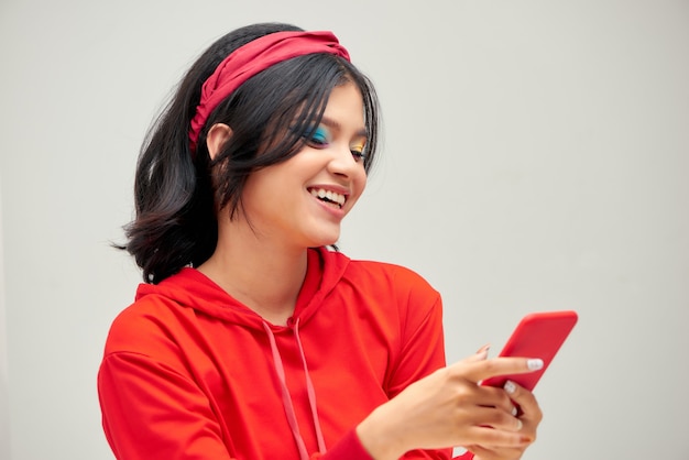 Bonita chica asiática encantadora charlando soñadoramente con su novio usando un teléfono inteligente aislado sobre fondo gris