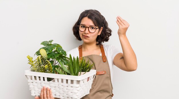 Bonita chica hispana haciendo capice o gesto de dinero diciéndote que pagues el concepto de plantas