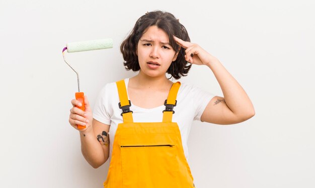 Bonita chica hispana que se siente confundida y perpleja mostrando que estás loco pintando el concepto de hogar