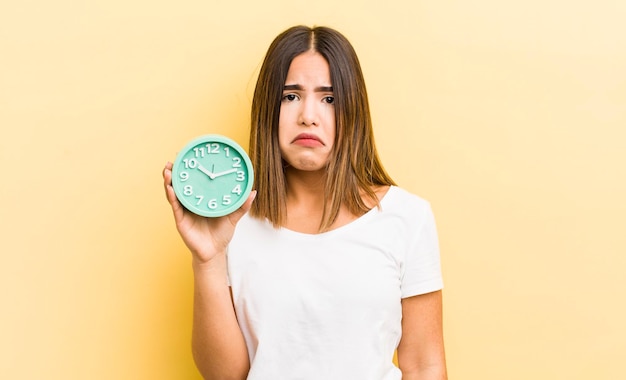 Bonita chica hispana que se siente triste y quejumbrosa con una mirada infeliz y un concepto de despertador llorando