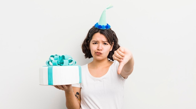 Bonita chica hispana sintiéndose cruzada mostrando los pulgares hacia abajo el concepto de cumpleaños