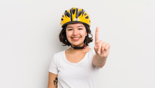 Bonita chica hispana sonriendo y luciendo amigable mostrando el concepto de bicicleta número uno
