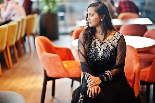 Bonita chica india con vestido de sari negro posado en el restaurante