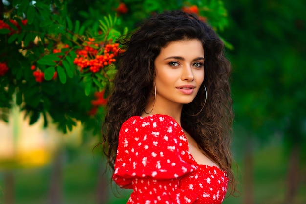 Foto bonita chica morena rizada con traje gitano rojo y accesorios posando en la naturaleza con serba