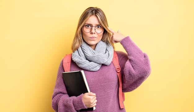 Bonita chica rubia que se siente confundida y perpleja mostrando que eres un concepto de estudiante loco