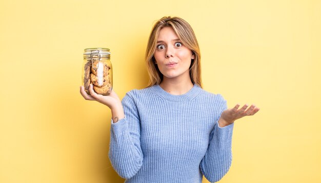 Bonita chica rubia que se siente perpleja, confundida y dudando. concepto de galletas caseras