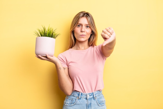 Bonita chica rubia sintiéndose cruzada mostrando los pulgares hacia abajo concepto de planta de interior