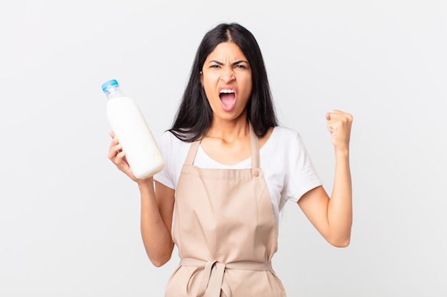 Bonita cocinera hispana gritando agresivamente con una expresión enojada y sosteniendo una botella de leche