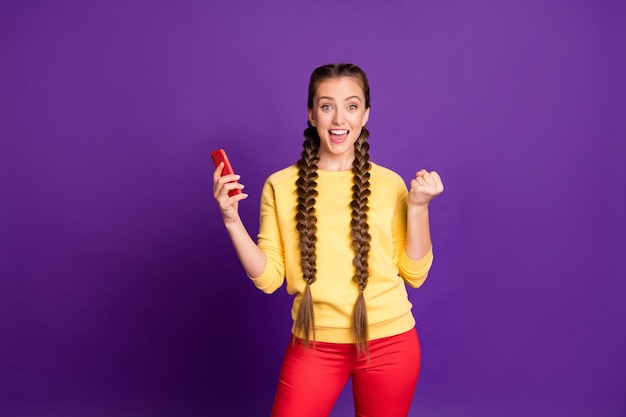 bonita dama adolescente trenzas largas sosteniendo teléfono ropa feliz casual suéter amarillo aislado pared de color púrpura