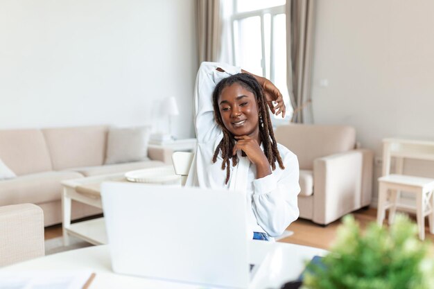 Bonita dama africana con el pelo negro trabajando en una laptop sentada en una mesa en casa, echa un vistazo a las tiendas en línea que venden el concepto de mujer tecnológica de los lunes cibernéticos para una oficina independiente alternativa