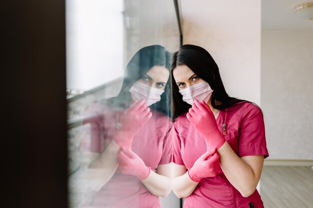 Bonita doctora poniéndose los guantes de látex en la clínica con grandes ventanas