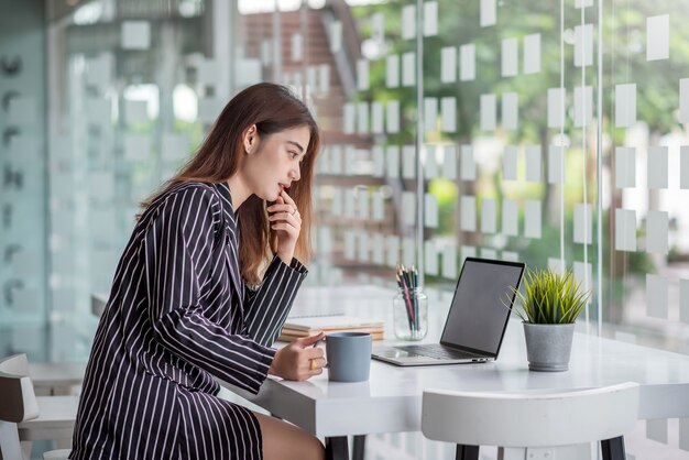 Bonita y encantadora mujer de negocios asiática que trabaja con una computadora portátil en un escritorio moderno