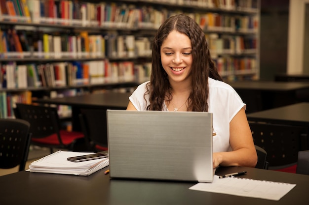 Bonita estudante universitária usando um laptop e fazendo alguns trabalhos de casa na biblioteca da escola