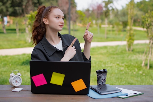 Foto bonita estudiante independiente sentada a la mesa en el parque usando una laptop