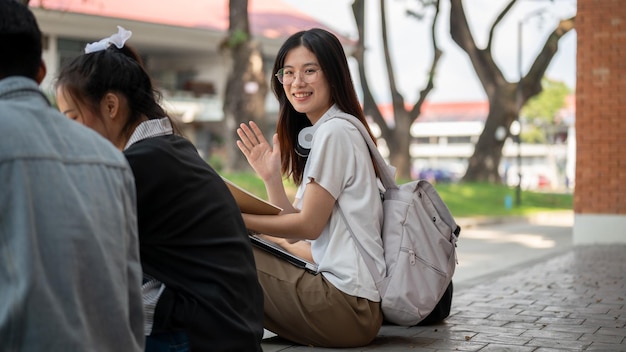 Una bonita estudiante universitaria asiática está sentada en una acera con sus amigas después de las clases