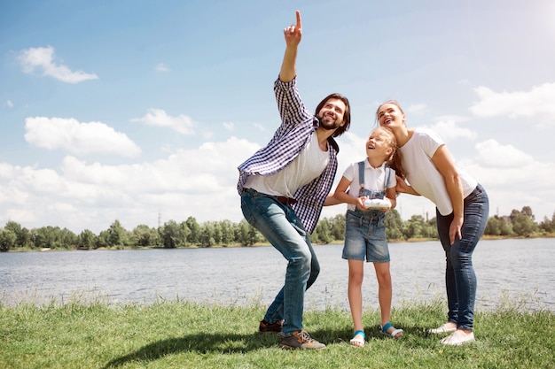 Bonita foto de familia joven mirando hacia arriba en el cielo. Guy está apuntando hacia arriba. La niña tiene un panel de control en las manos. Los padres están reteniendo a su hija. Son felices.