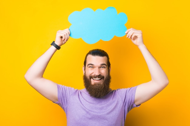 Una bonita foto de un joven con barba sosteniendo un bocadillo en forma de nube mientras mira a la cámara