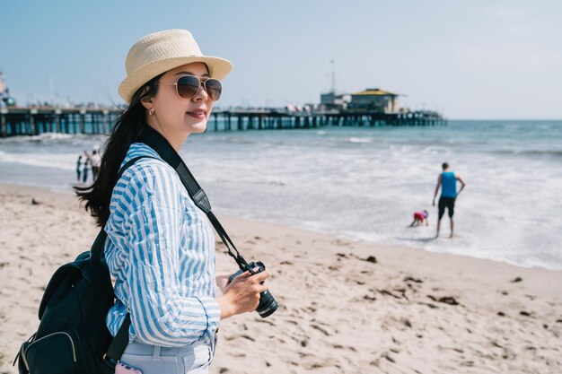 una bonita fotógrafa con gafas de sol y parada en la playa