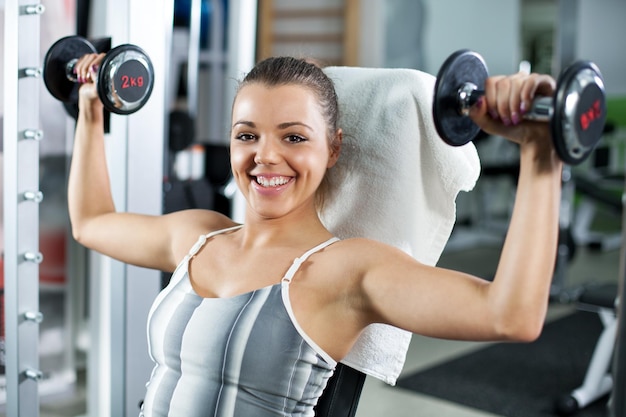 Bonita jovem desportiva fazendo exercício em um centro de fitness. Ela está trabalhando exercícios para fortalecer seu ombro.