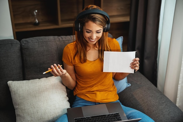 Bonita jovem estudante usando um laptop e fones de ouvido e aprendendo em casa.