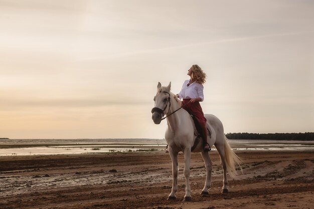 Bonita jovem feliz a cavalo na praia de verão à beira-mar