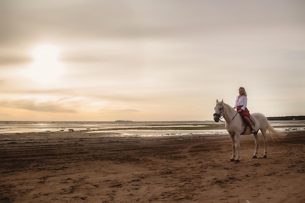Bonita jovem feliz a cavalo na praia de verão à beira-mar
