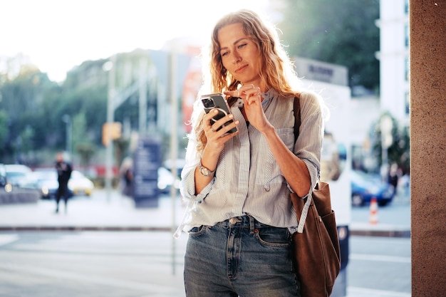 Bonita jovem sorridente com telefone celular andando na rua