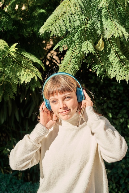 Una bonita joven caucásica escuchando música con auriculares azules en el parque