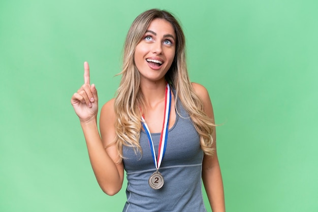 Bonita joven mujer uruguaya deportiva con medallas sobre un fondo aislado apuntando hacia arriba y sorprendida