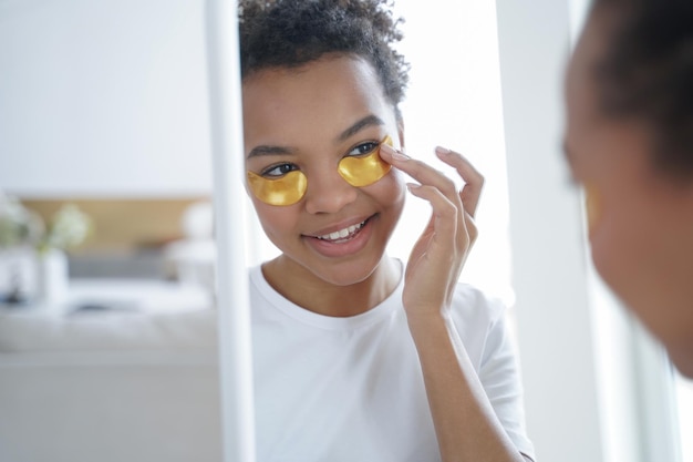 Bonita joven de raza mixta aplicando parches debajo de los ojos para el cuidado de la piel Publicidad de cosméticos de belleza