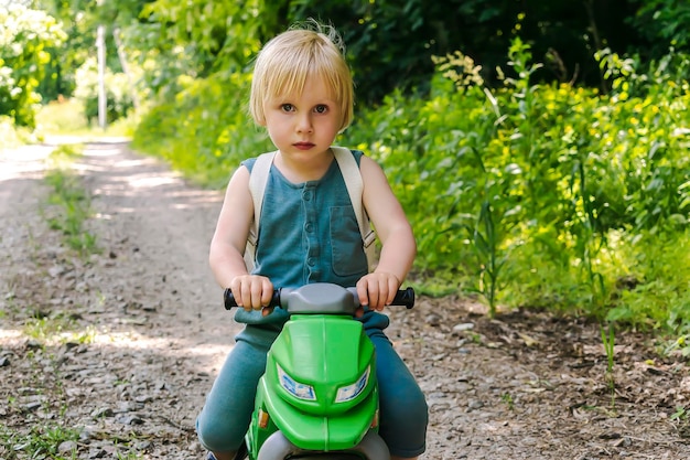 Bonita loira engraçada criança criança menino aprendendo a andar de bicicleta motocicleta de criança na estradaDesenvolvimento físico das crianças creche jardim de infância conceito paisagem rural natureza paisagem