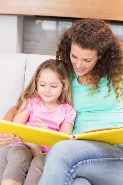 Bonita madre ayudando a su pequeña hija a leer un libro de cuentos