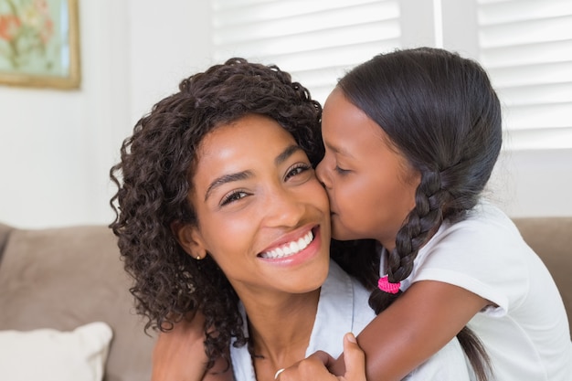 Bonita madre sentada en el sofá con su hija sonriendo a la cámara