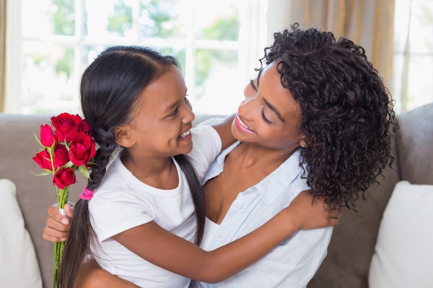 Bonita mãe sentada no sofá com a filha segurando rosas