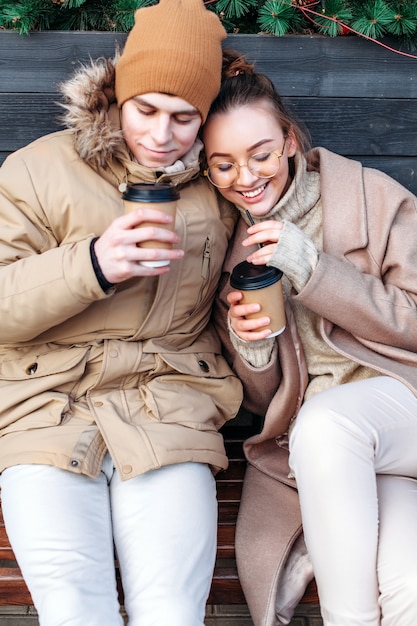 Bonita moda sensual elegante pareja de enamorados sentados en el banco en la calle en invierno, divirtiéndose juntos