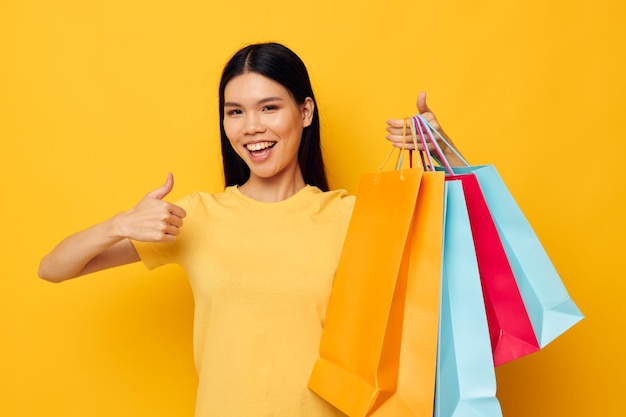 Bonita morena en una camiseta amarilla con bolsas de compras multicolores fondo amarillo inalterado