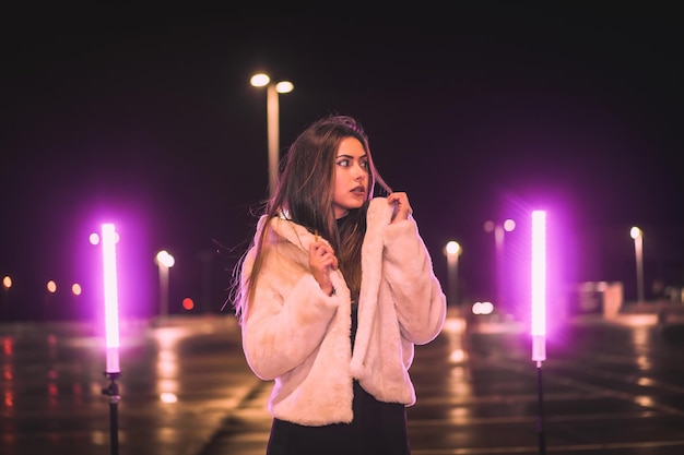 Bonita morena caucásica con una chaqueta de lana rosa en un aparcamiento vacío iluminado