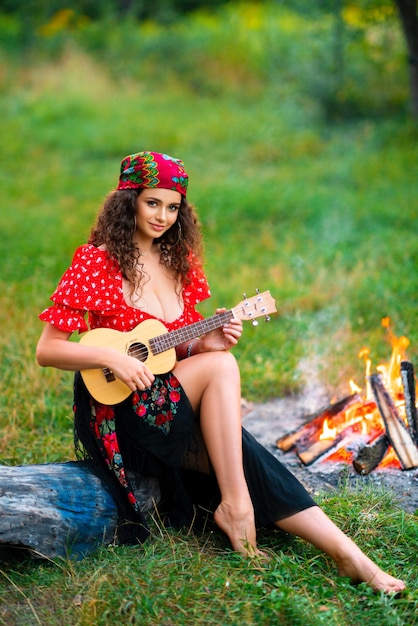 Foto bonita morena rizada con traje gitano rojo y accesorios tocando la guitarra