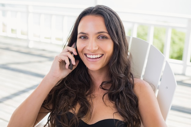 Bonita morena sentada en una silla y llamar con su teléfono móvil