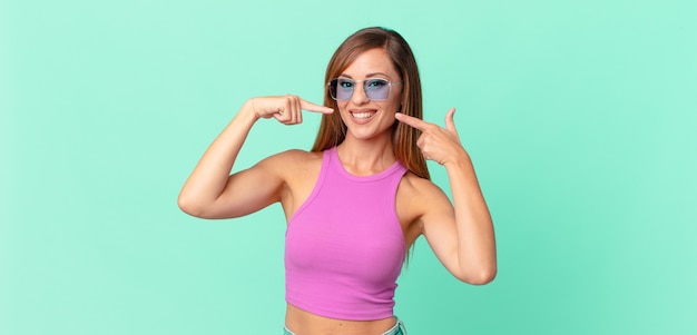 Bonita mujer adulta sonriendo con confianza apuntando a su propia amplia sonrisa