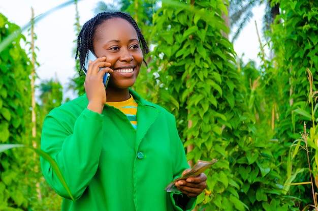 Bonita mujer africana en la granja haciendo llamadas en la granja mientras tiene dinero en la otra mano