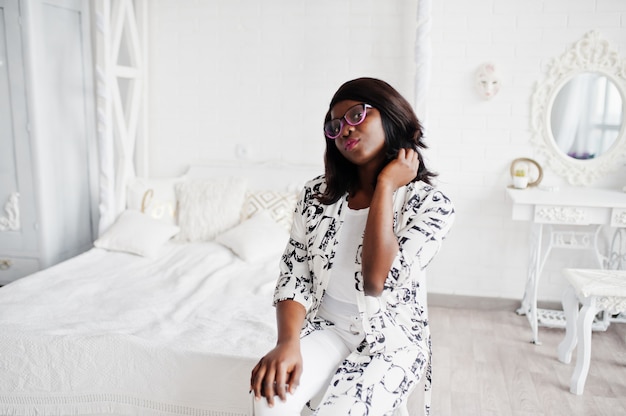 Bonita mujer afroamericana en anteojos, vestido blanco y negro presentado en la habitación.