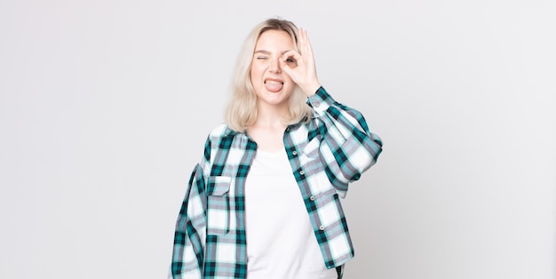 Bonita mujer albina sonriendo felizmente con cara divertida, bromeando y mirando por la mirilla, espiando secretos