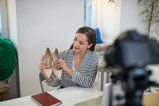 Bonita mujer alegre sosteniendo un par de zapatos delante de la cámara mientras les regalaban