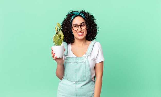 Bonita mujer árabe que parece feliz y gratamente sorprendida y sosteniendo un cactus en maceta