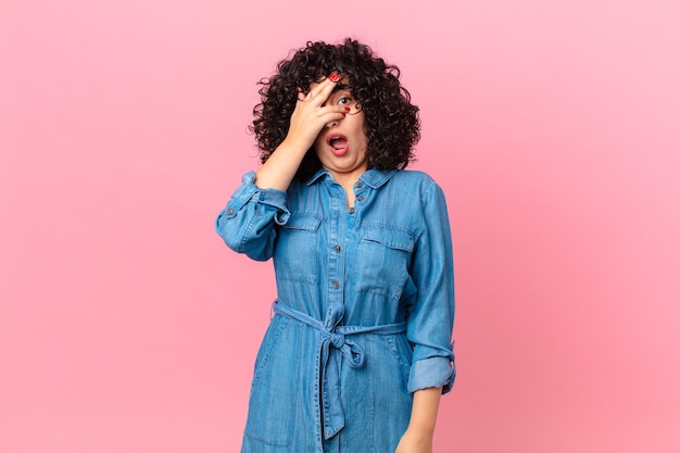 Bonita mujer árabe que parece sorprendida, asustada o aterrorizada, cubriéndose la cara con la mano